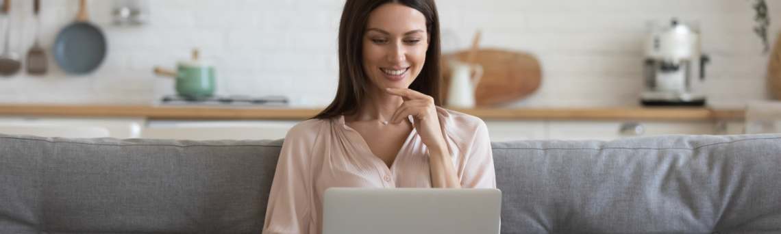 Woman sitting on couch looking at her laptop and smiling